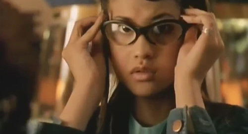 A screenshot from the film 'Tokyo Eyes' showing a young girl, Hinano (played by Hinano Yoshikawa), trying on a strange pair of thick glasses.